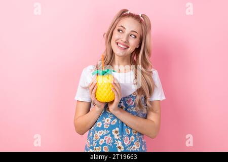 Foto di una ragazza simpatica e allegra che tiene in mano una tazza di bevanda all'ananas sembra uno spazio vuoto isolato su sfondo di colore rosa Foto Stock