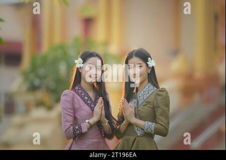Due giovani donne in abito tradizionale laotiano con le mani in posizione di preghiera Foto Stock