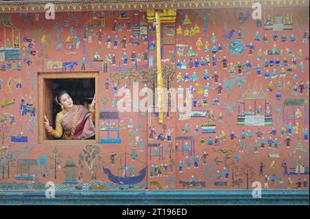 Donna che guarda fuori da una finestra aperta del tempio, Wat Xieng Thong, Luang Prabang, Laos Foto Stock