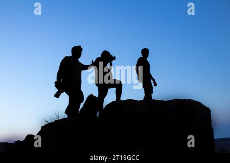 Silhouette di un gruppo di fotografi maschi in piedi o che scattano fotografie in cima alla montagna al tramonto serale con cielo blu sullo sfondo Foto Stock