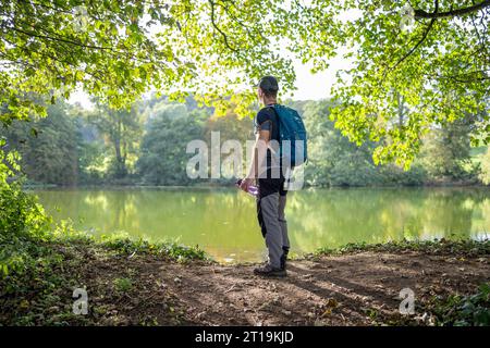 Vista posteriore dell'escursionista maschile/rambler con zaino sul retro, con serbatoio d'acqua e vista su un lago d'acqua dolce del Regno Unito in una calda e soleggiata giornata autunnale. Foto Stock