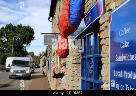 Lo spaventapasseri Spider-man fuori dal Deli Cafe durante il festival dello spaventapasseri del villaggio a Sharnbrook High Street, Bedfordshire, Inghilterra, Regno Unito Foto Stock