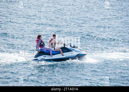 Un giovane uomo e una donna che si godono un giro su una moto d'acqua. Il passeggero si stende all'indietro rilassandosi mentre si muove lentamente in avanti verso il mare aperto Foto Stock