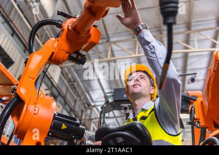 Uomo ingegnere moderno intelligente che utilizza la moderna tecnologia robotica. Configurazione del braccio di saldatura robotizzato nel processo di produzione dell'automazione in fabbrica Foto Stock