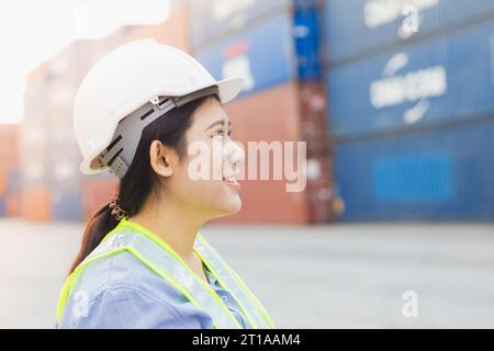 La donna asiatica lavoratrice di banchina felice controlla il carico dei container nei cantieri navali. Dipendente responsabile del personale marittimo e di trasporto. carico di carico per la spedizione da parte dell'operatore Foto Stock