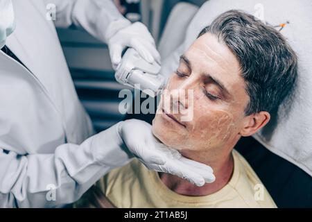 Medico della pelle che utilizza la tecnologia di trattamento viso viso con trattamento laser risurfacing con maschio adulto per ridurre rughe e cicatrici presso la clinica anti invecchiamento Foto Stock