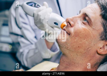 Medico della pelle che utilizza la tecnologia di trattamento viso viso con trattamento laser risurfacing con maschio adulto per ridurre rughe e cicatrici presso la clinica anti invecchiamento Foto Stock