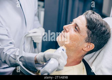 Medico della pelle che utilizza la tecnologia di trattamento viso viso con trattamento laser risurfacing con maschio adulto per ridurre rughe e cicatrici presso la clinica anti invecchiamento Foto Stock