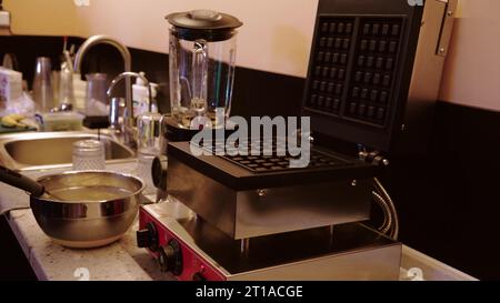Cucinare i waffle belgi in una macchina per waffle in una caffetteria. Primo piano di uno chef che versa l'impasto per waffle in una macchina per waffle in una cucina professionale Foto Stock