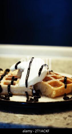 Condire i soffici waffle belgi con un condimento di cioccolato mentre prepari il dessert. Preparazione di dolci da waffle morbidi e gelati dolci Foto Stock