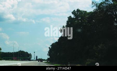 Vista attraverso il finestrino laterale di un'auto in movimento lungo la strada lungo la foresta in estate. Vista della foresta dal finestrino dell'auto. Turismo e viaggi, Foto Stock