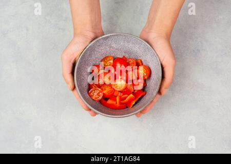 Pomodori e peperoni rossi a fette in una ciotola, preparare cibo sano con verdure di paprika, tenendo in mano la nutrizione biologica fresca Foto Stock