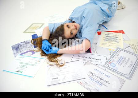 bella donna medico in guanti e tuta medica blu si trova sui diplomi certificati sul pavimento bianco formazione medica corsi di formazione medico infermiera dentista stomatologia alta qualifica Foto Stock