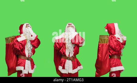 Stanco saint nick sbadiglia su sfondo verde, sentendosi stanco di portare zaino con regali e giocattoli per le vacanze della vigilia di natale. Babbo Natale si sente sonnolento in studio, vestito rosso. Foto Stock