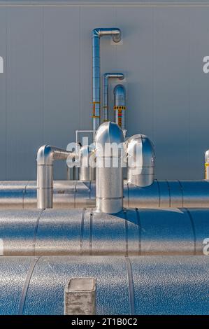 Tubazioni metalliche isolate riflettenti sul tetto di un impianto di stoccaggio a freddo (refrigerazione industriale), con tubazioni che attraversano una parete. Foto Stock