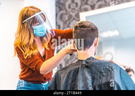 Apertura di saloni di parrucchiere dopo la pandemia di coronavirus, covid-19. Misure di sicurezza, maschera facciale, schermo protettivo, distanza sociale. Foto Stock