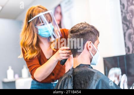 Apertura di saloni di parrucchiere dopo la pandemia di coronavirus, covid-19. Misure di sicurezza, maschera facciale, schermo protettivo, distanza sociale. Foto Stock