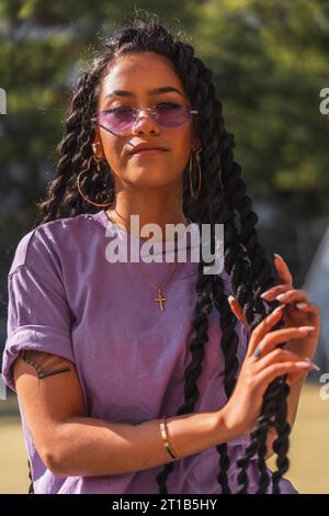 Giovane donna dalla pelle scura sorridente in camicia viola con trecce lunghe Foto Stock
