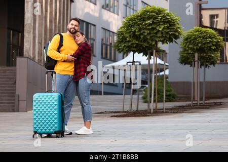 Relazione a distanza. Bella coppia giovane con bagagli che si abbracciano all'aperto Foto Stock
