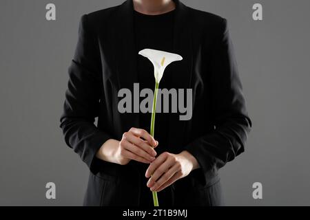 Donna con fiore di giglio di calla su sfondo grigio, primo piano. Cerimonia funebre Foto Stock