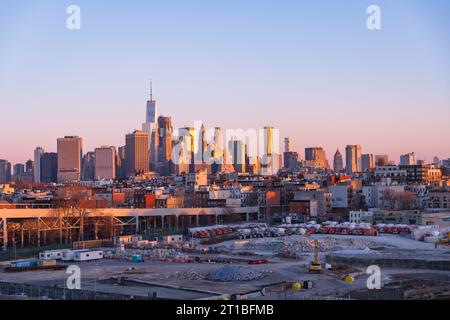 Vista dall'alto dei binari sopraelevati della metropolitana e del parcheggio di Brooklyn con lo skyline di Manhattan sullo sfondo all'alba Foto Stock