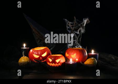 Composizione di Halloween con jack-o-lanterne, zucche, candele in fiamme e ragnatela su un tavolo di legno Foto Stock