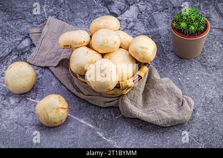 Un cestino rustico in vimini ripieno di funghi freschi adagiato su un ripiano in marmo. Foto Stock