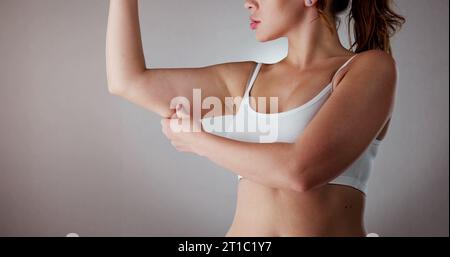 Close-up di una donna tenendo il braccio con un eccesso di grasso su sfondo grigio Foto Stock