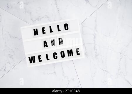 Salve e benvenuti scrivendo una scatola luminosa bianca su sfondo di marmo bianco. Foto Stock