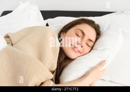 Ritratto di una bruna sorridente in pigiama, che dorme nel letto dell'hotel, che si rilassa con il viso contento, sogna, dorme in camera da letto Foto Stock