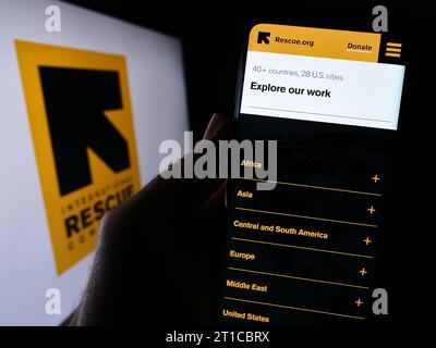 Persona in possesso di cellulare con pagina web dell'organizzazione International Rescue Committee (IRC) davanti al logo. Concentrarsi sul centro del display del telefono. Foto Stock