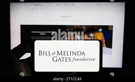 Persona che possiede uno smartphone con il logo dell'American Bill e della Melinda Gates Foundation (BMGF) davanti al sito Web. Concentrarsi sul display del telefono. Foto Stock