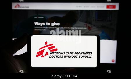 Persona che possiede uno smartphone con il logo dell'organizzazione benefica Doctors Without Borders davanti al sito Web. Concentrarsi sul display del telefono. Foto Stock