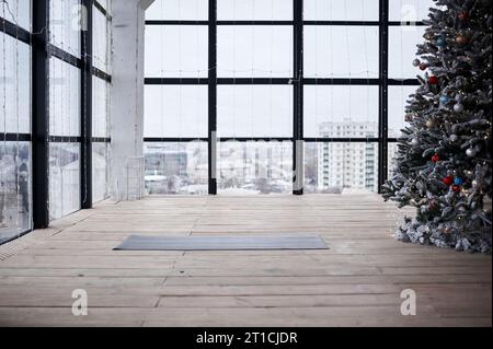 Spazio vuoto nel centro fitness, grandi finestre, pavimento in legno naturale, moderno monolocale loft, tappetino per yoga srotolato sul pavimento. niente persone. Celebrazione di Capodanno c Foto Stock
