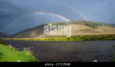 Vivaci archi a doppio arcobaleno sul maestoso paesaggio fluviale e montano Foto Stock