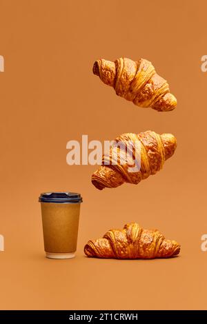 Levitare il cibo. Croissant freschi e croccanti sorvolano una tazza di caffè per accompagnarli su uno sfondo marrone. Foto Stock