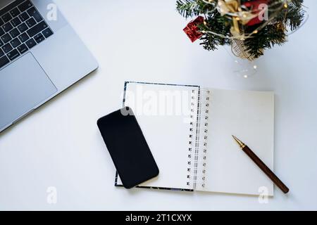 aprire il blocco note con un foglio vuoto per le risoluzioni del nuovo anno, i desideri o l'elenco delle attività. Laptop e smartphone in background Foto Stock