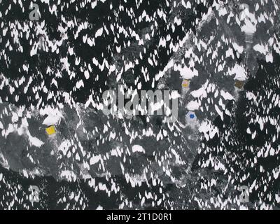 Tenda da da pesca gialla montata sul ghiaccio del lago. Superficie piana ghiacciata con rete di crepe, sponde di neve e cupola della tenda. Vista dall'alto verso il basso dell'antenna. Pesca invernale c Foto Stock