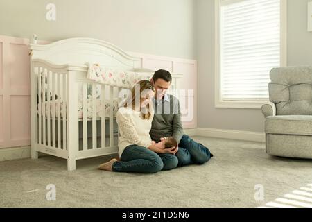 I nuovi genitori sono seduti sul piano dell'asilo, sorridendo alla bambina Foto Stock
