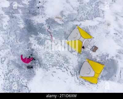 Pesca invernale su un lago ghiacciato. Tende da pesca colorate montate sul ghiaccio del lago. Vista aerea. Foto Stock