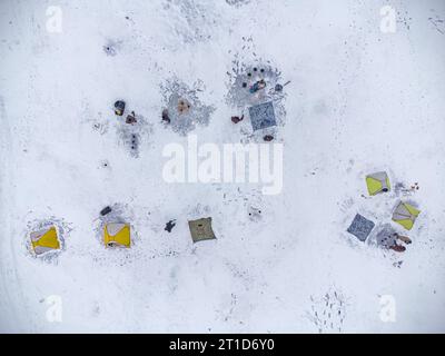 Pesca invernale su un lago ghiacciato. Tende da pesca colorate montate sul ghiaccio del lago. Vista aerea. Foto Stock