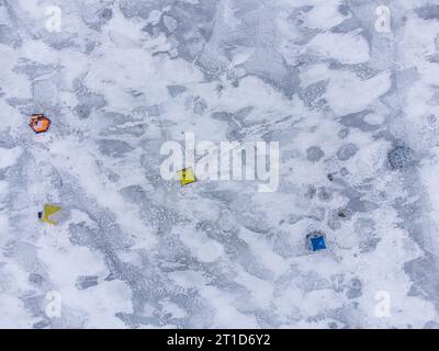 Pesca invernale su un lago ghiacciato. Tende da pesca colorate montate sul ghiaccio del lago. Vista aerea. Foto Stock