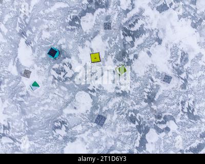 Pesca invernale su un lago ghiacciato. Tende da pesca colorate montate sul ghiaccio del lago. Vista aerea. Foto Stock