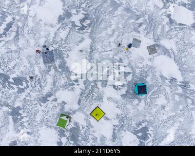 Pesca invernale su un lago ghiacciato. Tende da pesca colorate montate sul ghiaccio del lago. Vista aerea. Foto Stock