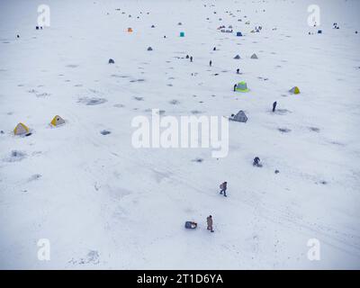 Pesca invernale su un lago ghiacciato. Tende da pesca colorate montate sul ghiaccio del lago. Vista aerea. Foto Stock