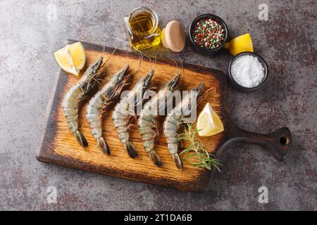 Gamberetti di tigre nera crudi non sbucciati, gamberi con limone, erbe e spezie primo piano sulla tavola di legno su un tavolo. Vista superiore orizzontale dall'alto Foto Stock