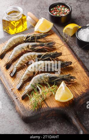 Gamberetti di tigre neri freschi non cotti con ingredienti marinati da vicino su un tagliere sul tavolo. Verticale Foto Stock