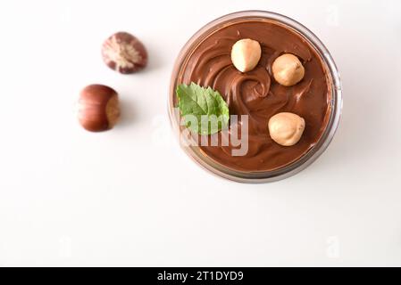 Crema di cacao con nocciole in una ciotola di vetro con frutta e foglia isolata su tavola bianca. Vista dall'alto. Foto Stock