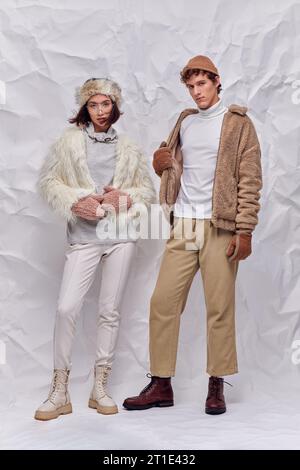 coppia interrazziale con cappelli, guanti caldi e giacche in pelliccia sintetica su sfondo bianco increspato Foto Stock