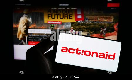 Persona che possiede uno smartphone con il logo dell'organizzazione internazionale di beneficenza ActionAid davanti al sito Web. Concentrarsi sul display del telefono. Foto Stock